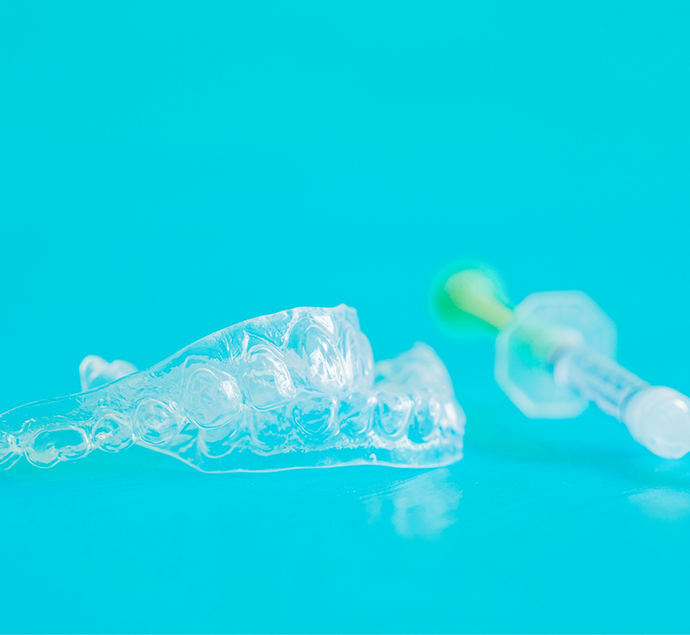 Two clear teeth whitening trays next to an applicator for gel