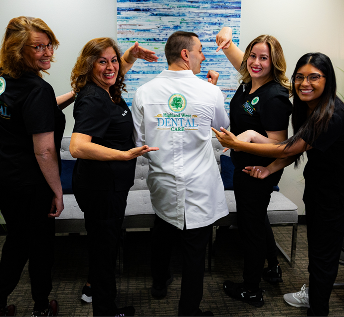 Dental team members pointing to Doctor Pevzner and the Highland West Dental Care logo on the back of his white lab coat