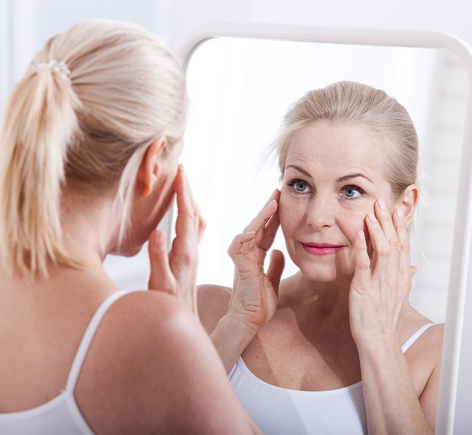 Mature woman looking at herself in mirror, concerned about wrinkles