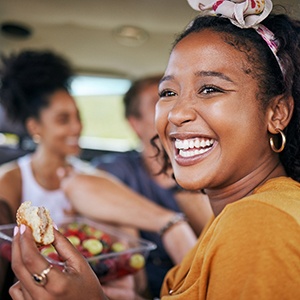 Woman smiling while eating lunch with friends on road trip