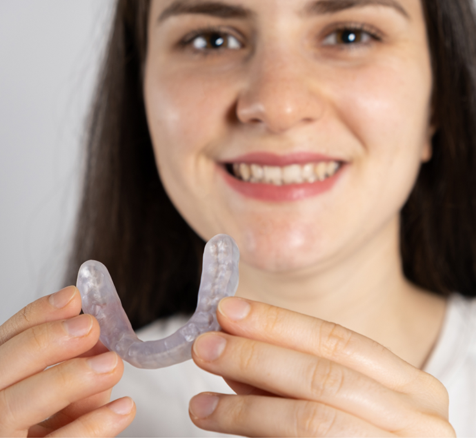 Smiling woman holding a clear T M J tray for her teeth