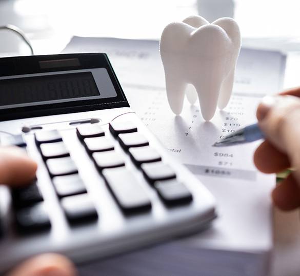 Hands pressing calculator keys and holding pen at desk with invoice and model tooth