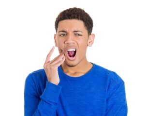 Young man holding side of face with mouth open looking surprised and worried.