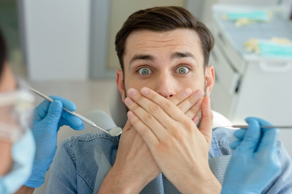 A scared man covering his mouth at the dentist.